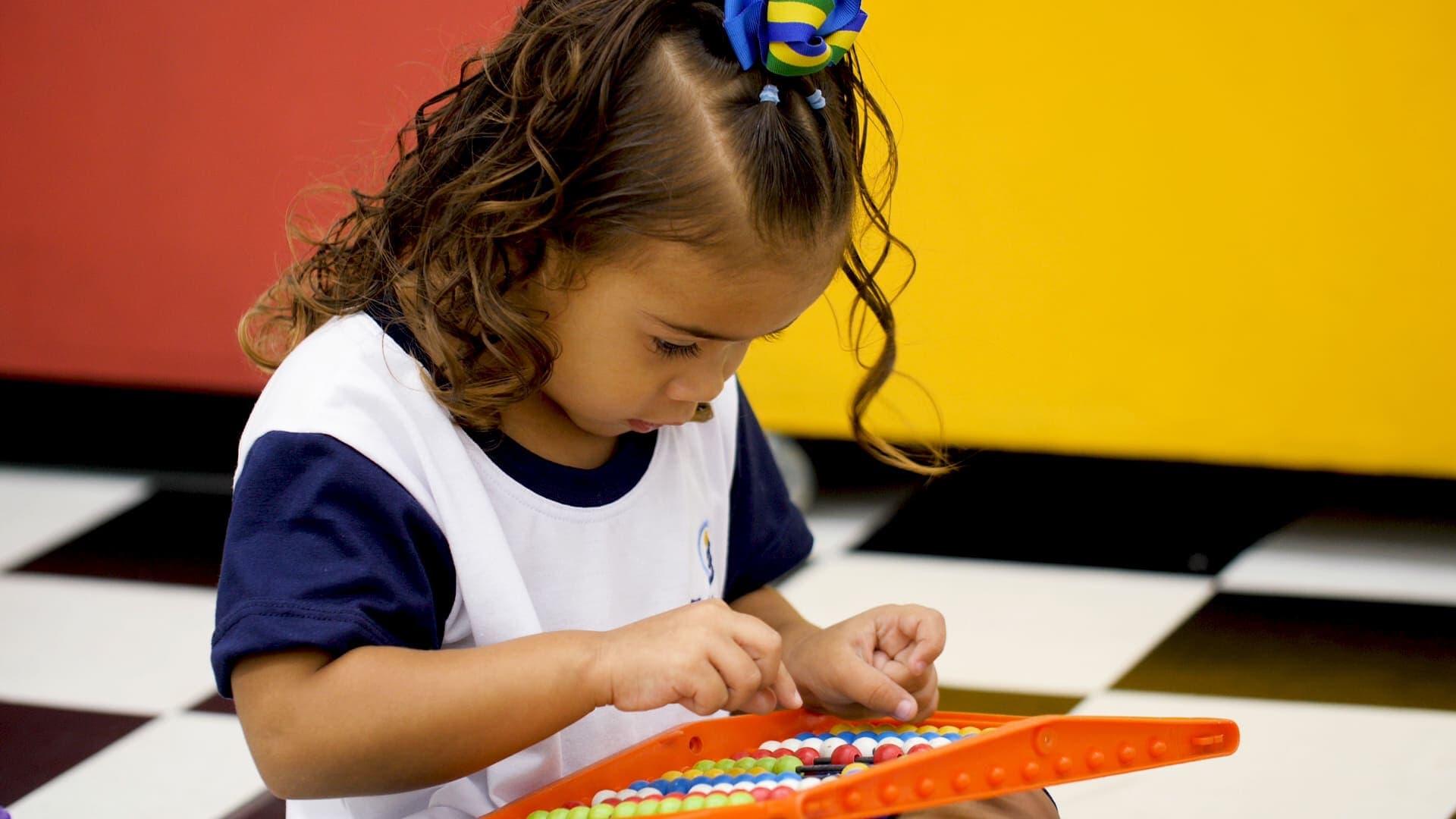 Criança concentrada manuseia um brinquedo educativo com peças coloridas, desenvolvendo atividade de coordenação motora.
